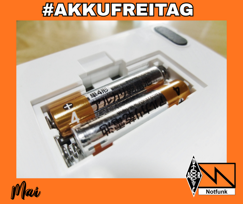 Offenes Batteriefach eines weißen Geräts mit zwei eingelegten AA-Batterien, oben der Schriftzug ‚#AKKUFREITAG‘, unten links ‚Mai‘, rechts das DARC- und Notfunk-Logo auf orangefarbenem Rahmen.