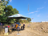 Die Feldtagsstation unter einem Sonnenschirm, dahinter der UKW-Antenne.