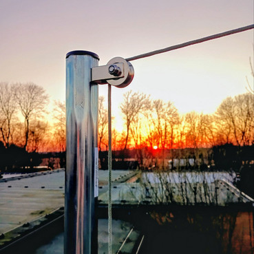 Ein Seil liegt über einer Umlenkrolle, die an einem Mast befestigt ist. Im Hintergrund geht die Sonne in rötlichen Farben unter.